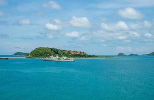 Neben einer kleinen Insel liegen militärische Kriegsschiffe. vor dem hintergrund der grünen berge und des klaren himmels im golf von thailand, sattahip, thailand. foto