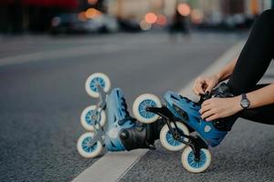 Beine einer nicht erkennbaren Frau zieht Rollschuhe an, die Übungen im Freien haben, führt aktive Lifestyle-Posen auf der Straße, bereitet sich auf Inline-Skating vor. Der gesichtslose Skater betreibt gefährlichen Sport foto