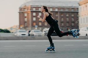 sportliche Frau fährt auf Rollen bewegt sich sehr schnell in aktiver Kleidung gekleidet genießt Rollerblading und wird in Aktionsposen an städtischen Orten fotografiert, die Extremsport betreiben. aktives Lifestyle-Konzept foto