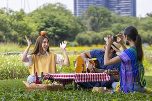 Eine Gruppe junger, vielfältiger enger Freunde, die im Garten picknicken, während sie im Sommer fröhlich und glücklich Musik im öffentlichen Park im Freien singen foto