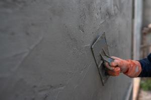 detailliertes Nahaufnahmefoto eines Zementarbeiters, der eine Kelle verwendet, um die Wände zu verputzen foto