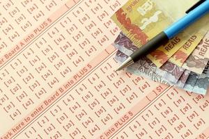 Stift mit brasilianischen Geldscheinen auf dem Lotteriespiel. Konzept von Glück und Glücksspiel in Brasilien foto