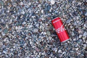 Die ursprüngliche rote Blechdose von Coca Cola liegt auf kleinen runden Kieselsteinen in der Nähe der Küste. Coca-Cola am türkischen Strand foto