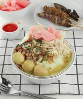 bubur ayam oder indonesischer reisbrei, serviert mit geschnetzeltem hähnchen, kuchen, chili und hochwertigen eiern. selektiver fokus foto