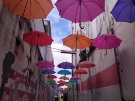 ein ummauerter Flur, der mit bunten Regenschirmen geschmückt ist. Dieses Foto kann für alles verwendet werden, was mit Tourismus, Stadt, urbanem Leben, Kunst und Architektur zu tun hat