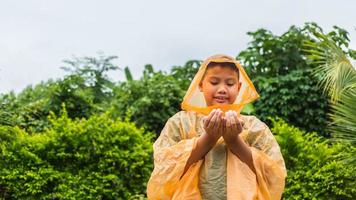 Der asiatische Junge mit orangefarbenem Regenmantel ist glücklich und hat Spaß im Regen an einem regnerischen Tag. foto