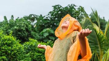 Der asiatische Junge mit orangefarbenem Regenmantel ist glücklich und hat Spaß im Regen an einem regnerischen Tag. foto