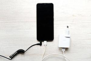 Modernes Smartphone mit eingesteckten Strom- und Audiokabeln auf dem Tisch foto