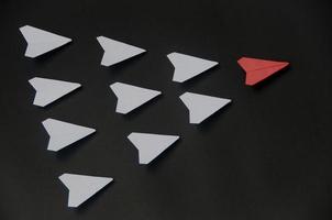 rotes papierflugzeug origami führende weiße flugzeuge auf dunklem hintergrund. konzept für führungskompetenzen foto