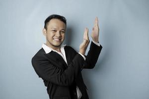 Aufgeregter asiatischer Mann im Anzug, der auf den Kopierraum über ihm zeigt, isoliert durch blauen Hintergrund foto