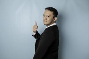Aufgeregter asiatischer Geschäftsmann im Anzug gibt Daumen nach oben Handgeste der Zustimmung, isoliert durch blauen Hintergrund foto