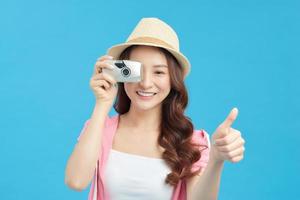 Porträt eines lächelnden hübschen Mädchens im Kleid, das ein Foto auf einer Kamera macht, die über blauem Hintergrund isoliert ist