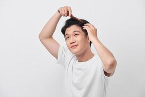 Schönheits-, Pflege- und Leutekonzept - lächelnder junger Mann, der Haare mit Kamm über weißem Hintergrund bürstet foto