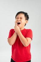 asiatische Erscheinung des kleinen Jungen in einem roten Hemd eine Hand zu ihrem faltigen Gesicht der Wange auf einem weißen Hintergrund, Zahnschmerzen retro foto