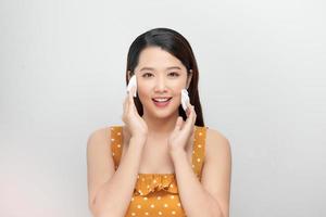 Schönheitsporträt einer lächelnden Frau mit weicher, gesunder Haut, die Make-up mit einem Wattepad entfernt, das über weißem Hintergrund isoliert ist foto