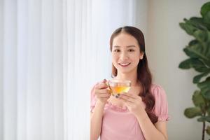 Schöne Frau mit einer Tasse Tee, die in der Nähe des Fensters steht foto