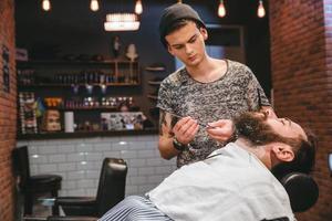 Friseur rasiert bärtigen Mann mit Rasiermesser