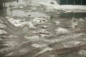 schlammige Pfütze aus geschmolzenem Schnee auf der Straße. ungereinigter Parkplatz. foto