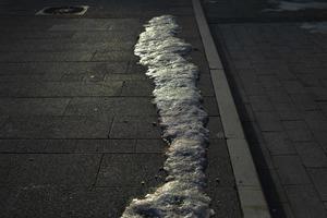 Schnee schmilzt auf der Straße. Eis auf der Oberfläche des Tratoirs. foto