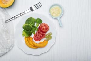 Gesundes Essen Brokkoli-Tomaten-Kürbis-Salat in weißer Platte auf Holzhintergrund. foto