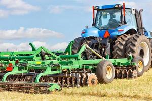 Ein leistungsstarker landwirtschaftlicher Traktor, der an einem Sommertag mit einer mehrreihigen Scheibenegge gekoppelt ist. foto