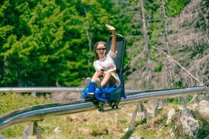 Mädchen fährt Bergachterbahn und Wellen. Bergwelt mit Bäumen im Hintergrund foto