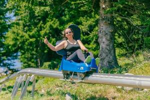 Frau mit Sonnenbrille fährt mit erhobenem Daumen auf einer Bergachterbahn. warmer Sommertag auf dem Berg foto