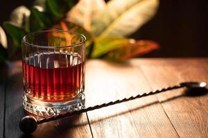 facettiertes Glas Whiskey mit Cocktaillöffel auf einem Holztisch foto