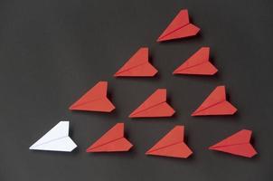 weißes papierflugzeug origami führende rote flugzeuge auf dunklem hintergrund. konzept für führungskompetenzen foto