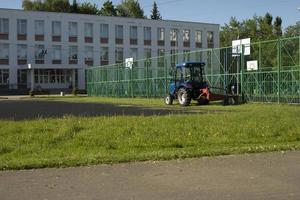 Traktor mäht Gras außerhalb der Schule. Säuberung des Territoriums. foto