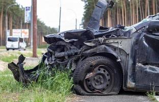 Schwarzes Auto nach einem schrecklichen Unfall am Straßenrand. Frontal- und Seitenaufprall. Lebensversicherung. ein Unfall ohne Heilungsmöglichkeit. Seitenansicht. Schäden nach einem Unfall. foto