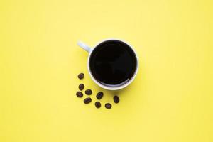 schwarzer kaffee in einer tasse und kaffeebohnen auf gelbem hintergrund. Kopierbereich von oben. foto