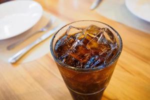 Cola-Glas-Erfrischungsgetränk mit Eis auf Holztisch im Restauranthintergrund foto
