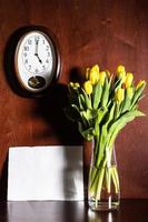 Wanduhr, leeres Papier und Tulpen in der Vase foto