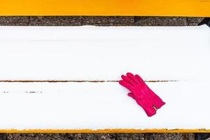 Roter Handschuh auf gelber Holzbank mit Schnee bedeckt foto