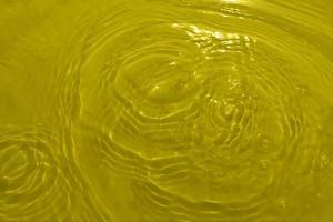 Unscharfe, transparente, gelb gefärbte, klare Wasseroberflächenstruktur mit Spritzern und Blasen. trendiger abstrakter naturhintergrund. wasserwelle im sonnenlicht mit kopierraum. gelbes aquarell glänzt. foto