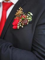 die Hochzeits-Boutonniere des Bräutigams aus Sukkulenten und roten Blumen in einer schwarzen Jacke mit roter Krawatte. festliche Dekoration, Blumen, Kleidung für die Heiratsurkunde. Nahaufnahme, Platz für Text foto