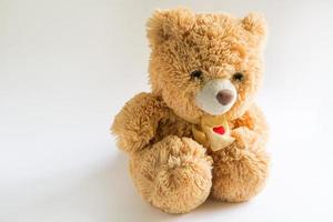 Weicher Teddybär mit langem hellbraunem Fell und einem roten Herz auf einem Schal um den Hals. Valentinstagsgeschenk, Kinderspielzeug. weißer Hintergrund, Platz für Text foto