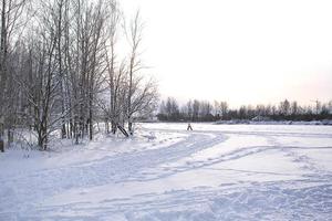 Winterlandschaft - weißer Schnee mit Spuren von Schuhen und Skiern auf dem Feld. die Skipiste und die Straße, die den Wald mit kahlen Bäumen umsäumen, sanftes Sonnenlicht. foto