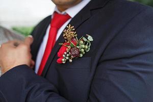 die Hochzeits-Boutonniere des Bräutigams aus Sukkulenten und roten Blumen in einer schwarzen Jacke mit roter Krawatte. festliche Dekoration, Blumen, Kleidung für die Heiratsurkunde. Nahaufnahme, Platz für Text foto