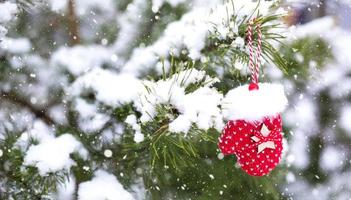 rotes weihnachtsspielzeug gestrickte fäustlinge auf zweig der natürlichen fichte, die mit schnee bedeckt ist. neues jahr im freien. Schneefall, Girlandenlichter, festliche Stimmung von Märchen und Magie, Straßendekoration. Platz kopieren foto