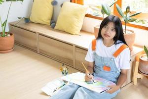 junges Mädchen, das auf dem Boden sitzt und zu Hause auf Papier malt. Hobby und Kunststudium zu Hause. foto