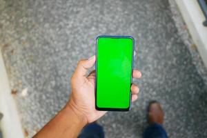 POV der Hand eines jungen Mannes mit Smartphone mit grünem Bildschirm foto