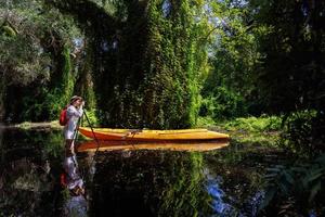 Forscherin oder Botanikerin verwendet eine Kamera auf einem Stativ, um die Vegetation in einem Feuchtwald zu fotografieren. Touristin steht in einem Sumpf und fotografiert neben einem Kanu. foto