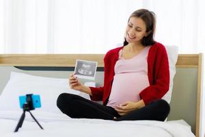 schöne schwangere kaukasische frau zeigt glücklich ein ultraschallbild in einem videoanruf über ein smartphone. foto