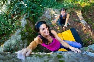 Fröhliches Mädchen, das Bouldern mit dem Sturzpad übt, und ihr Partner schützt sie im Falle eines Sturzes foto