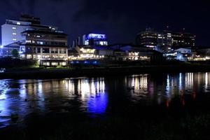 Kamo-Fluss bei Nacht. moderne und traditionelle Gebäude mit Restaurants, Bars, Hotels. junge Leute am Ufer für angenehme Atmosphäre. glattes Wasser durch lange Belichtung. foto