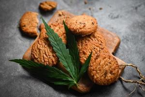 Cannabis-Lebensmittelkekse mit Cannabisblatt-Marihuana-Kraut auf hölzernem und dunklem Hintergrund, köstlicher süßer Dessertkeks mit Hanfblattpflanze thc cbd-Kräuter-Nahrungsmittelsnack und medizinisches Konzept foto