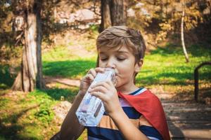 Durstiger Junge trinkt Wasser aus einer Flasche im Park. foto