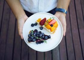 Nahaufnahme von Frauenhänden, die einen Teller mit Blaubeerkuchen und Mango mit Erdbeertorte im hausgemachten Bäckereistil halten foto